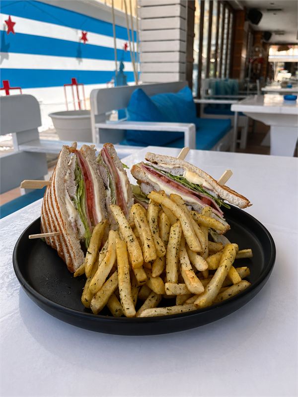 Toasted club sandwich quarters with chicken, ham, lettuce and tomato, with herbed fries on a black plate
