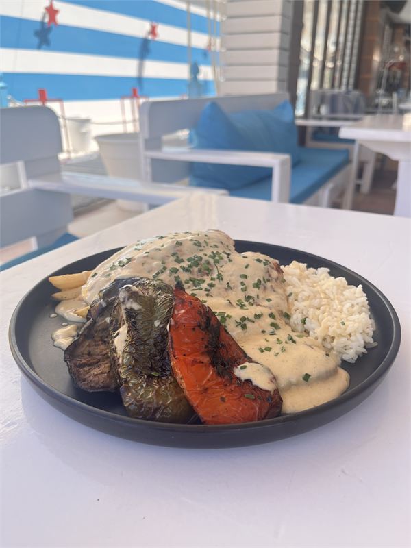 Grilled fillet under a creamy sauce with chives, with rice, grilled peppers and aubergine on a black plate