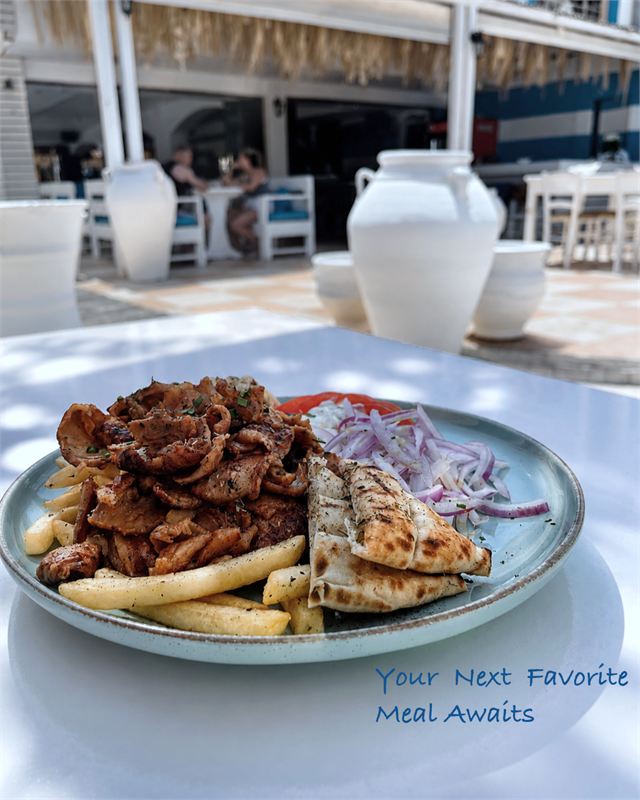 A gyros plate with grilled pita, red onion, tomato, tzatziki and fries on a pale blue plate on the terrace
