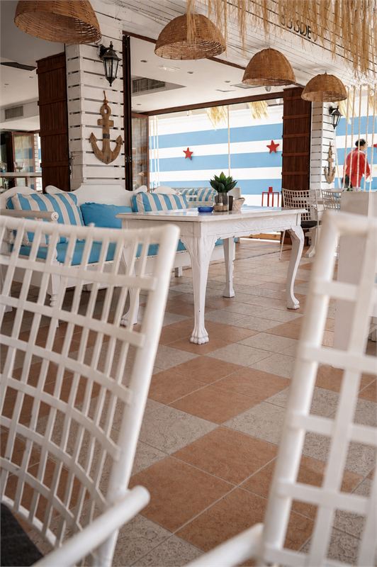 Inside Ocean: a wooden anchor on a white slatted pillar, rattan lamps and a white sofa with striped cushions