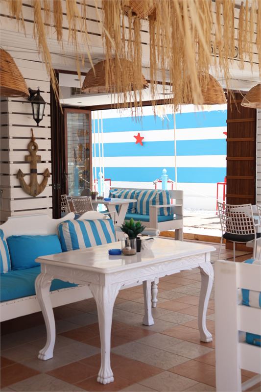 A lounge corner with a carved white table, blue-and-white striped cushions and the striped wall with a starfish outside