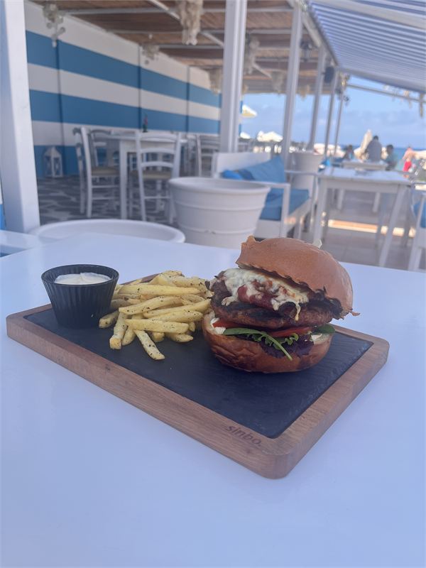 A burger with melted cheese, bacon, tomato and rocket in a brioche bun, served on slate with fries and a dip