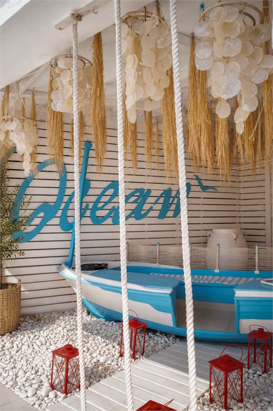 The painted Ocean sign on a white slatted wall above a blue-and-white wooden boat, with red lanterns on white pebbles