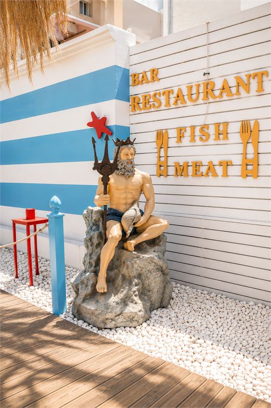 Poseidon statue seated on a rock beside the Bar Restaurant Fish Meat sign at the entrance