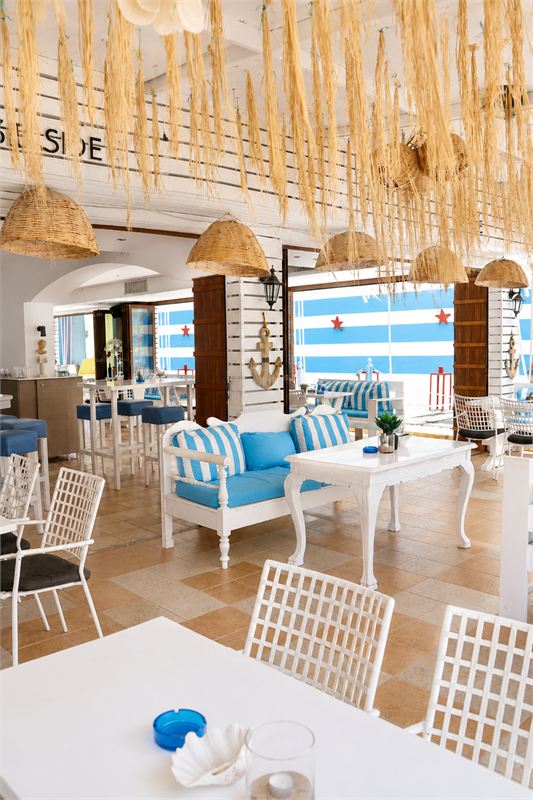 The Seaside lounge inside Ocean: raffia lampshades, a white carved sofa with blue-and-white striped cushions and the striped wall beyond