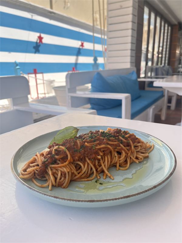 Spaghetti bolognese topped with fresh basil on a pale blue plate, blue-and-white striped wall behind
