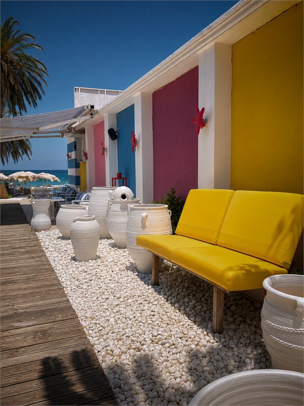The Ocean terrace: a yellow lounge seat, white clay pots on pebbles and a wooden deck leading to the sea and a palm tree